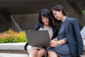Two businesswoman working together with laptop in front of their office building  
