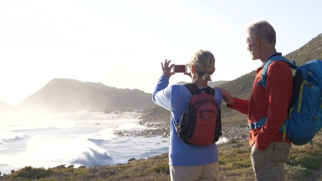 Mature hikers stopping to take photos overlooking the sea
