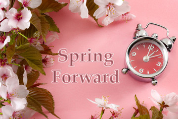 Turn clocks on hour ahead, star of daylight savings time change and reminder to spring forward concept with alarm clock on pink background with springtime flowers and text - spring forward