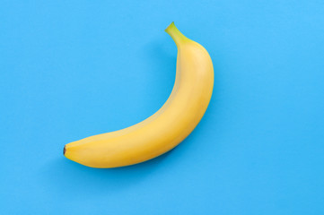 Minimalist pattern, fresh fruit and colorful art concept with flat lay top view of single yellow banana isolated on bright blue background