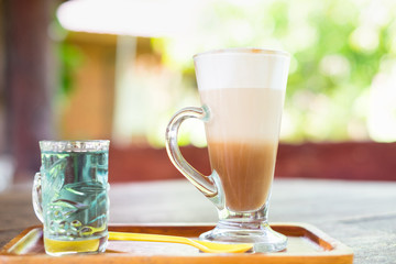 Cappuccino layer coffee on wooden dish and fresh butterfly pea water soft focus blurred background.vintage tone.