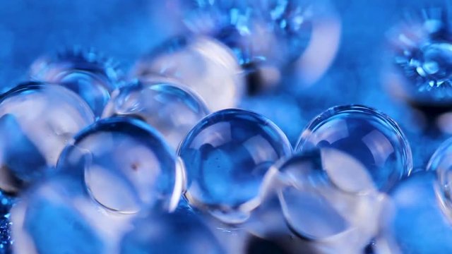 Crystal Gel water balls on blue glitter texture rotation. Close up macro footage.