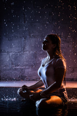 Obraz premium Girl with wet hair in the white shirt, water drops around and dark wall background illuminated by light