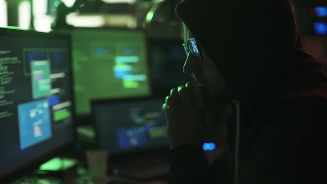 Hacker with hoodie working with multiple screens and hacking systems