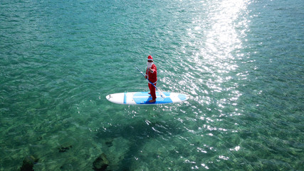 Aerial drone of Santa Claus paddle surfing in Caribbean turquoise clear waters