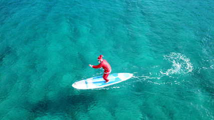 Aerial drone of Santa Claus paddle surfing in Australian emerald sea water