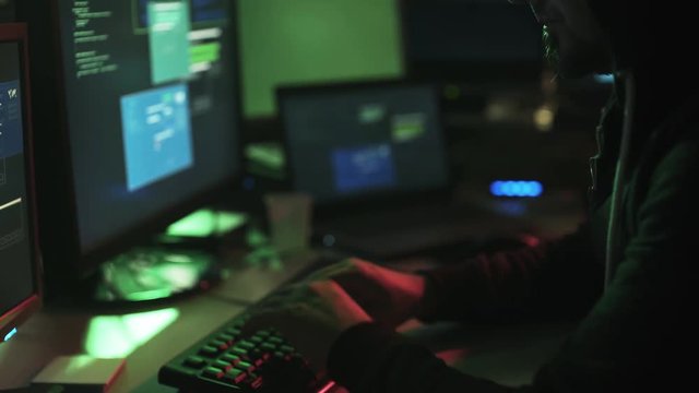Hacker with hoodie working with multiple screens and hacking systems