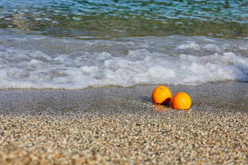 Naklejka premium Oranges lie on the sand. Waves from the sea are rolling ashore