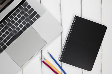 Laptop pc, black color notebook paper  and red, yellow,blue color pencil on white wooden table background with copy space for text. Lady desk office idea and concept.minimal style