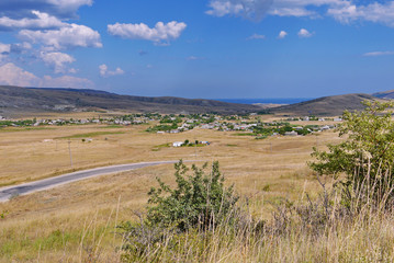 Outdoor landscape. Valley with a yellow dried grass and hills under a bright blue sky. And here is a small town