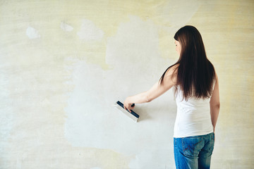 Woman plastering the walls with finishing putty in the room.