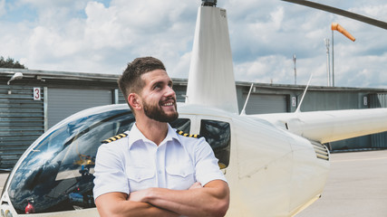 Portrait of commercial pilot in uniform standing near small private helicopter on a landing point © supamotion