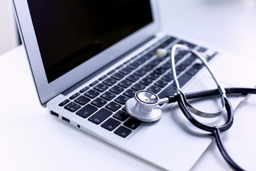 Obraz na płótnie Canvas Stethoscope lying on a laptop keyboard in a concept of online medicine or troubleshooting the computer viewed low angle with copy space