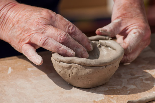 closeup of hands of old woman making clay pottery bowl in outdoor