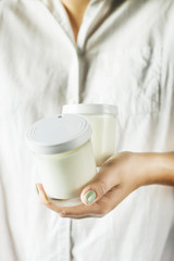 Two glass jars with homemade yogurt in the hands of a woman in a white shirt. Healthy diet breakfast