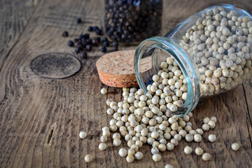 Dried white and black pepper corns with glass bottle on wooden background.