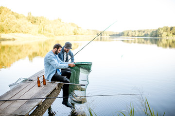 Deux amis masculins heureux regardant le filet de pêche avec du poisson pendant la pêche sur le lac