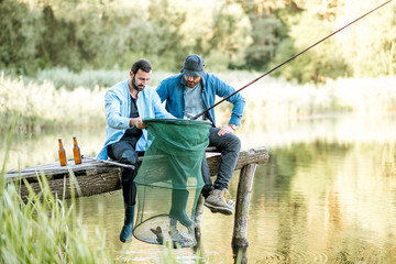 Deux amis masculins heureux regardant le filet de pêche avec du poisson pendant la pêche sur le lac