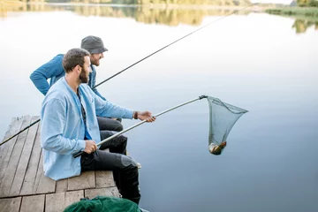 Photo sur Plexiglas Pêcher Two friends catching fish with fishing net and rod sitting on the wooden pier at the lake