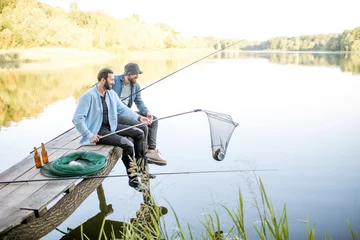 Photo sur Plexiglas Pêcher Deux amis attrapant du poisson avec un filet de pêche et une canne assis sur la jetée en bois au bord du lac