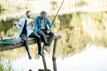 Sierkussen Twee gelukkige vissers die gevangen vis vasthouden terwijl ze op de houten pier zitten tijdens het vissen op het meer in de ochtend © rh2010