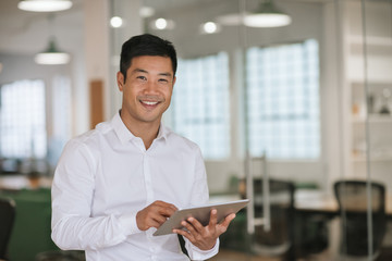 Smiling Asian businessman using a digital tablet in an office - obrazy, fototapety, plakaty