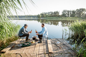 Landscape view on the lake with two male friends sitting together with beer during the fishing process