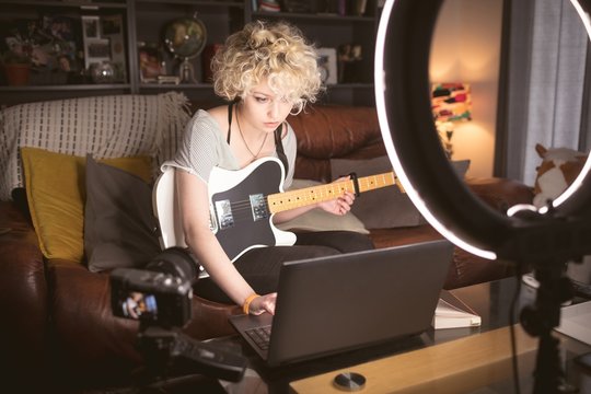 Female blogger with guitar using laptop in living room