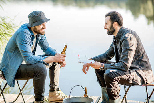 Two fishermen sitting together with beer while fishing on the lake at the morning