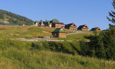 Fototapeta na wymiar Wooden houses with decks with green tile roofs on hills of the same color