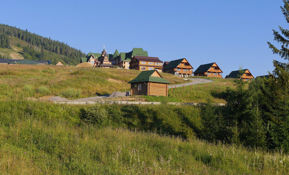 Wooden houses with decks with green tile roofs on hills of the same color