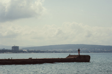 Fototapeta premium Fisherman with a fishing rod on a sea pier in the background of the city