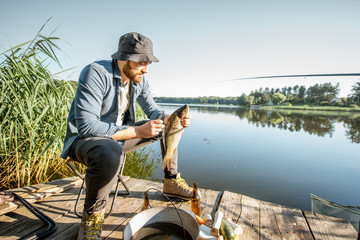 Portrait d& 39 un beau pêcheur avec du poisson sur la jetée en bois près du lac le matin