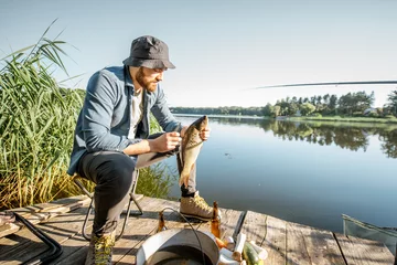 Photo sur Plexiglas Pêcher Portrait d& 39 un beau pêcheur avec du poisson sur la jetée en bois près du lac le matin
