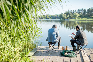 Landscape view on the beautiful lake and green reeds with two men fishing on the wooden pier during the morning light