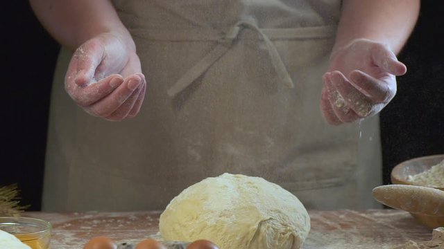 Female clapping hands and sprinkling flour over fresh dough on kitchen table