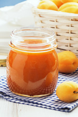 Apricot jam in a glass with apricots on a light background. Copy space.