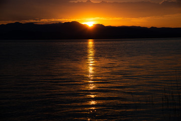 Sunrise Over Lake And Mountains. Early morning landscape. mountain in  silhouettes and the red rays of the rising sun. Sunrise on Lake Garda, Italy