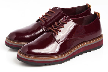 Deep red shiny pair of shoes on a white background.