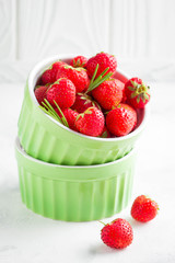Small strawberry in green cup, fresh juicy summer berry on light background, home garden