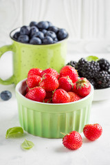 Fresh blueberries, strawberries, blackberries in cups, juicy summer berry on light background, home harvest, garden