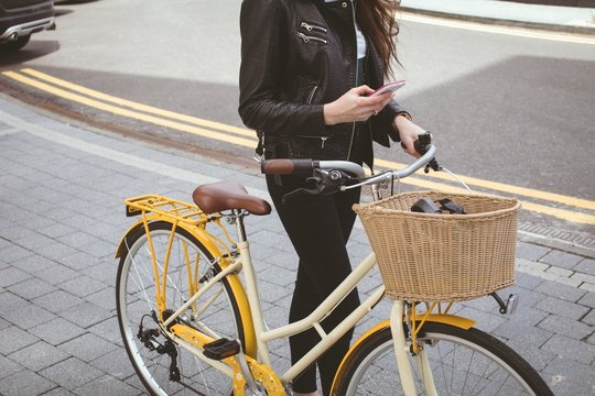 Low section of woman holding bicycle while using mobile phone