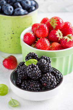 Fresh blueberries, strawberries, blackberries in cups, juicy summer berry on light background, home harvest, garden