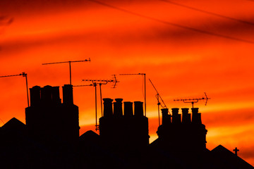 chimneys, tv ariels and telephone lines on terraced houses against orange sunset