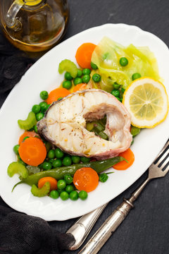 boiled fish with boiled vegetables and lemon on white dish