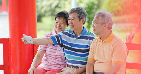 Senior friends talk together and take selfie with mobile phone at outdoor park