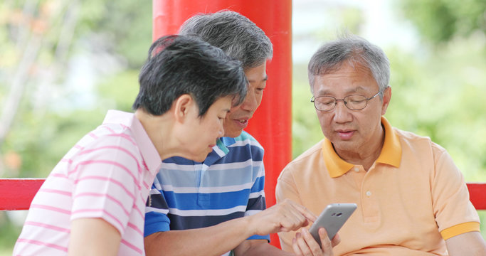 Senior friends talk together look at mobile phone at outdoor park