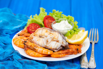 boiled fish with shrimps and salad on white dish on blue background