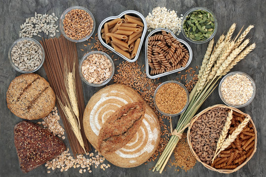 Food high in dietary fibre with whole grain bread and seeded rolls, whole wheat pasta, seeds, cereals and grains on marble background top view. Foods high in antioxidants, omega 3 and vitamins. 