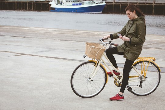 Woman on bicycle using mobile phone at harbor